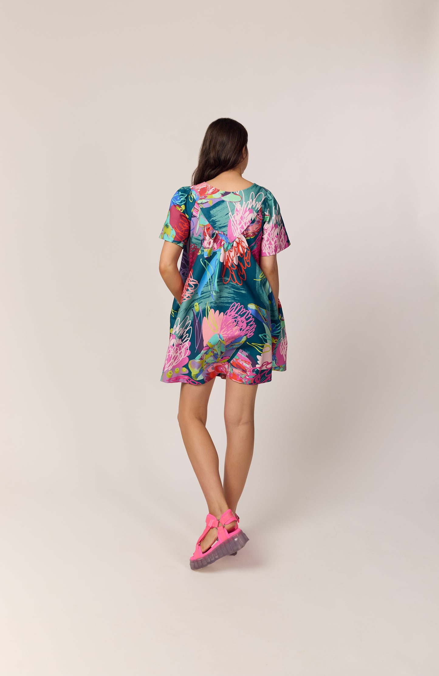 Back view of The Debut Dress in Protea Collage – colourful organic cotton dress in bold collage pattern, teal base, floral print, painterly details and pops of neon.